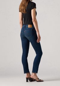 Jeans in denim blu scuro con una silhouette aderente, completati da una toppa in pelle marrone chiaro nella parte posteriore dei fianchi, e tacchi neri slim.