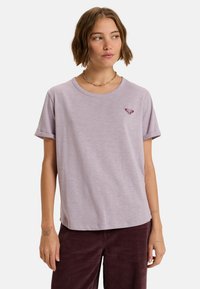 Lavendelkleurig T-shirt met korte mouwen, ronde halslijn en opgerolde mouwen. Voorzien van een klein donker hartlogo boven de linkerborst. Zachte textuur.