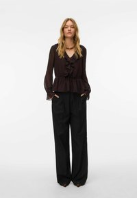Blouse en chiffon noir avec col volanté et manches longues, taille cintrée, associée à un pantalon noir taille haute à jambes larges.