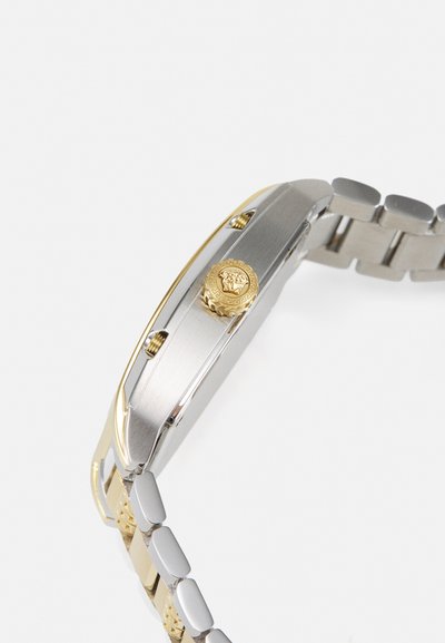 Relógio de pulso em aço inoxidável com uma coroa e detalhes em dourado. Apresenta uma bracelete em metais mistos, forma retangular elegante e acabamento liso.