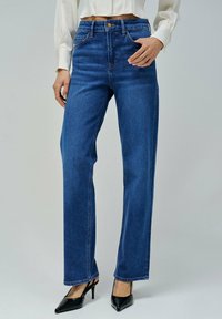 Jeans rectos de tiro alto en azul, con cierre de botón, cinco bolsillos y costuras en contraste. Llevados con tacones negros de punta. 