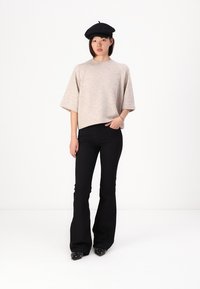 Pulover tricotat bej cu mânecă scurtă, asortat cu pantaloni negri evazați. Beretă neagră, pantofi negri cu accente argintii. Look simplu și relaxat.