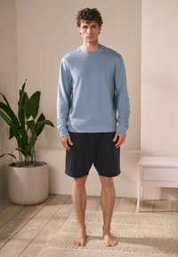 Lichtblauwe sweatshirt met lange mouwen gecombineerd met marineblauwe korte broek. Voorzien van een ronde hals en een comfortabele, losse pasvorm. Soepele textuur met minimale details.