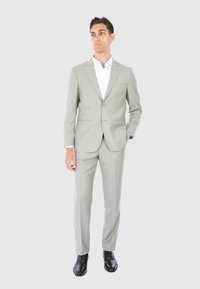 Suit verde chiaro con un solo bottone, rever a punta e vestibilità slim. Abbinato a una camicia bianca e scarpe in pelle nere.