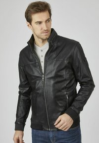 Chaqueta de cuero negra con cremallera frontal, dos bolsillos laterales, puños acanalados y cuello alzado. Textura suave y corte elegante.