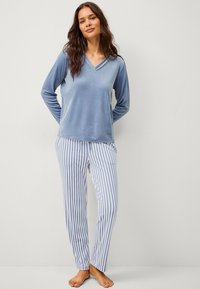 Lichtblauw velours top met lange mouwen en een V-hals, gecombineerd met witte en blauwe gestreepte pyjamabroek. Zachte textuur en een relaxte pasvorm.