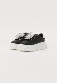 Svarte plattformsneakers med teksturert skinnoverdel, hvit chunky såle og dekorative lys grå stoffblomsterdetaljer på snøringen.