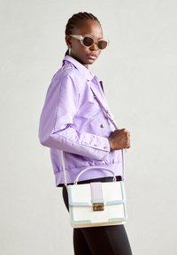 Fialová bomberová bunda, černé legíny a vícebarevná kabelka. Kabelka má texturovaný povrch, zlaté kovové doplňky a nastavitelný popruh.