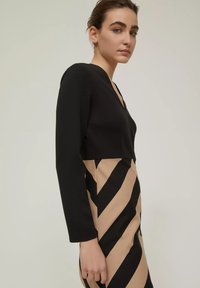 Abito lungo nero a maniche lunghe con scollo a V, caratterizzato da una parte inferiore beige con strisce nere diagonali. Tessuto morbido, design aderente.