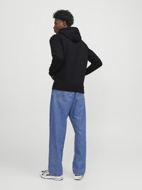Black hooded sweatshirt, relaxed fit, paired with loose blue denim jeans. Distinct textured fabric and white sneakers complete the look.