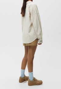 Cremefarvet ribstrikket langærmet skjorte med knapmanchetter, kombineret med tan-farvede shorts, lyseblå sokker og beige sneakers med plateau. Enkel og afslappet stil.