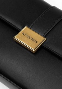 Portafoglio in pelle nera con un accento hardware rettangolare dorato in cui è impresso la parola "WITTCHEN". Texture liscia con dettagli cuciti.