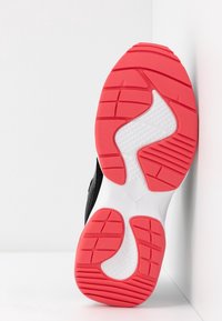 Podešev černého sportovního boty s červeným a bílým texturovaným gumovým vzorkem na bílém pozadí.