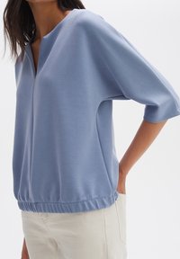 Maglione azzurro chiaro con scollo a V, maniche a 3/4 e orlo elastico. Tessuto liscio con una leggera lucentezza; design a vestibilità rilassata.