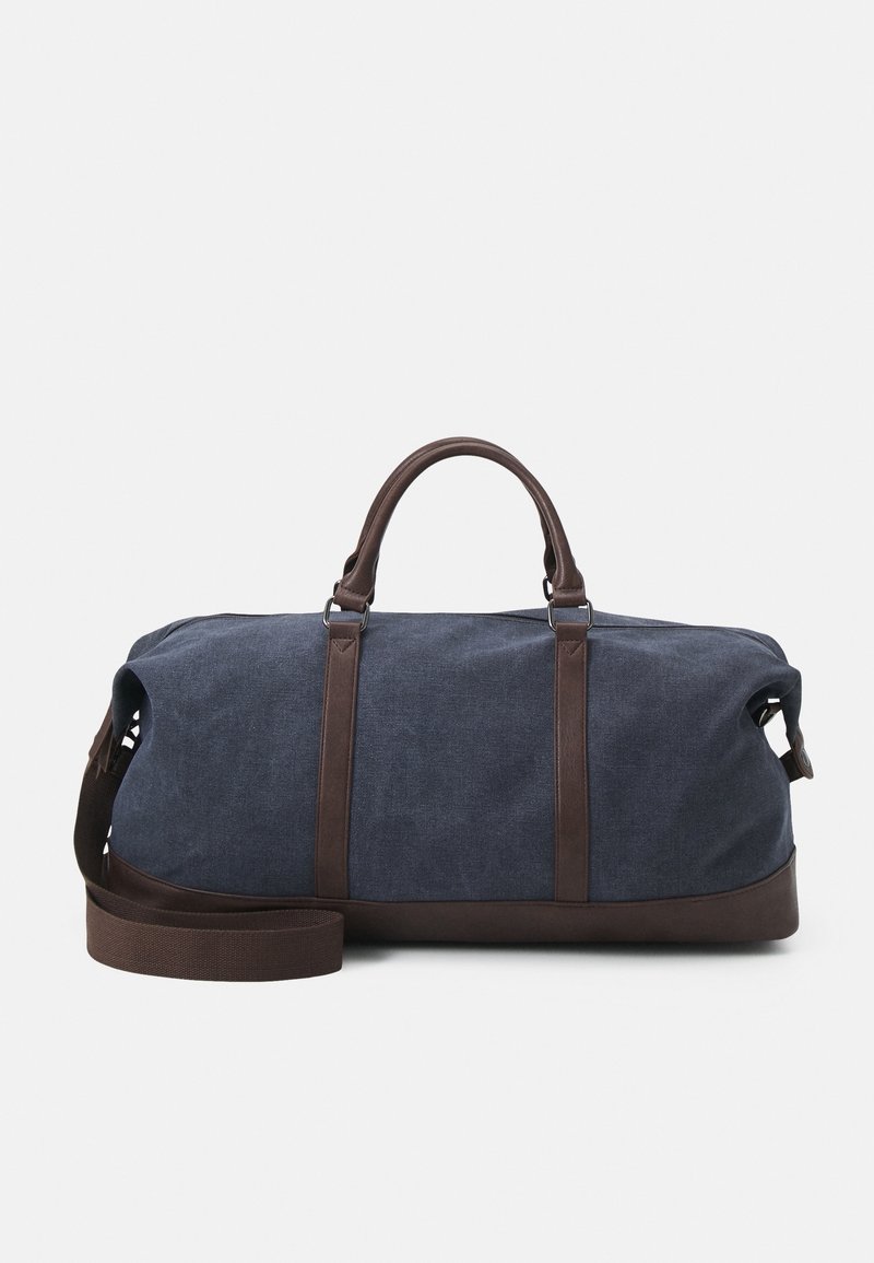 Sac de sport en toile bleu marine avec des accents en cuir marron, doté de poignées doubles et d'une bandoulière amovible, de forme structurée et de texture lisse.