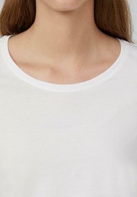 Weißes T-Shirt aus glattem Baumwollmaterial mit klassischem Rundhalsausschnitt, das einen weichen Stoff ohne sichtbare Muster oder Akzente zeigt.
