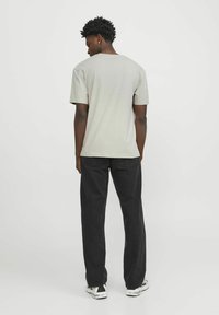 Camiseta de algodón gris claro con cuello redondo y mangas cortas, combinada con jeans negros de pierna recta y zapatillas blancas.