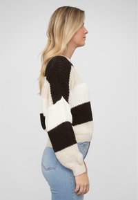 Strickpullover in beige und dunkelbraunen Streifen. Verfügt über einen runden Halsausschnitt, weite Bündchen und einen lockeren Schnitt. Weiche Textur, ausgeprägter Farbkontrast.