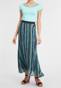 Top azul claro con escote recortado, combinado con una falda larga y fluida que presenta rayas verticales en azul, verde y negro. Sandalias de cuña marrones.