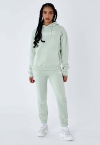 Sudadera verde menta con un bolsillo frontal y cordón, combinada con pantalones jogger a juego. Presenta puños acanalados y detalles de logotipo bordado.