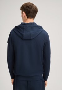 Marineblaue Kapuzen-Sweatshirt aus weichem Stoff, mit lockerer Passform, gerippten Bündchen und einem dezenten Logodetail am Ärmel.