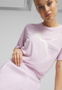 Svetlo vijoličasta športna majica s kratkimi rokavi in belim logotipom Puma na sprednji strani, v kombinaciji s podobno obarvanimi trenirkami.
