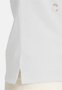 Hvid bomulds t-shirt med en sideslids, der har en lille glitrende pink rhinestone 'C' detalje på forsiden. Glat tekstur, afslappet pasform.