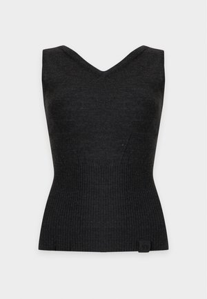 Donna in piedi di fronte, indossa un top nero senza maniche con scollo a V, pantaloni neri a gamba larga e tacchi neri aperti su uno sfondo bianco uniforme.