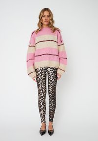 Rosa und cremefarbener gestreifter Pullover mit übergroßen Ärmeln, kombiniert mit Leggings im Leoparden-Muster. Schwarze spitze High Heels runden das Outfit ab.