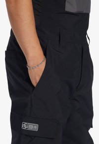 Zwarte cargobroek van lichtgewicht materiaal met zakken en een logo-opdruk. Heeft een slim fit en gedetailleerde stiksels.