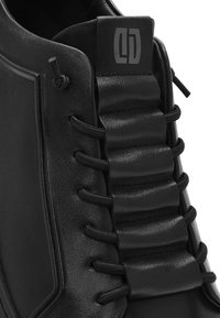 Scarpa in pelle nera con un design a plissé imbottito, lacci elasticizzati e un logo impressa sulla linguetta per un tocco di dettaglio in più.