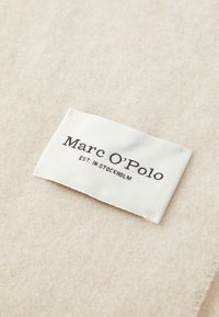 Marc O’Polo geweven label op beige textielmateriaal, met de merknaam en de tekst "EST. IN STOCKHOLM".