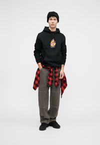 Μαύρη φούτερ μπλούζα με γραφικό λογότυπο, γκρι φαρδιά παντελόνια και κόκκινο καρό πουκάμισο δεμένο στη μέση. Ένα μαύρο σκουφάκι και αθλητικά παπούτσια ολοκληρώνουν την εμφάνιση.