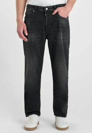 Zwarte spijkerbroek van denim met een rechte snit, voorzien van versleten details, vijf-pocketdesign en een knoopsluiting, gedragen met witte sneakers.