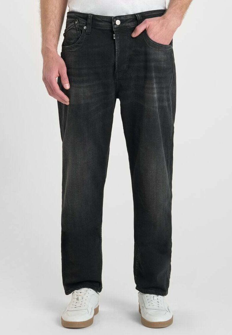 Jean en denim noir à coupe droite, avec des détails déchirés, un design à cinq poches et une fermeture à bouton, portés avec des baskets blanches.