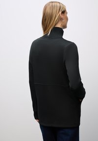Maglione nero con un colletto alto e a costine, maniche lunghe e una texture morbida; presenta una cucitura sul retro e tasche ai lati.