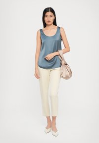 Light blue satin sleeveless top, cream tapered pants, brown bag with knotted handle, and pointed white shoes. Smooth textures and clean lines.