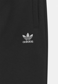 Schwarze Jogginghose aus Baumwollmischung, mit einem gestickten grauen Adidas-Logo und dem dreistreifigen Blättern-Design auf dem linken Oberschenkel.