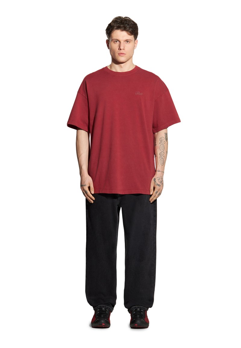 Czerwona, oversize koszulka z bawełny, z krótkimi rękawami. Połączona z luźnymi czarnymi spodniami i czarno-czerwonymi trampkami. Prosty design, bez wzorów.