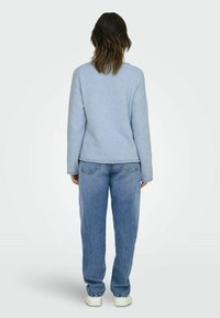 Jasnoniebieski sweter o teksturowym wzorze z długimi rękawami, zaokrąglonym dołem i luźnym krojem, zestawiony z dżinsami prostymi w średnim odcieniu oraz białymi trampkami.