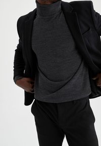 Ciemnoszary golf pokazany pod czarną marynarką, cechujący się gładką fakturą i luźnym krojem, z subtelnymi zdobieniami na mankietach.