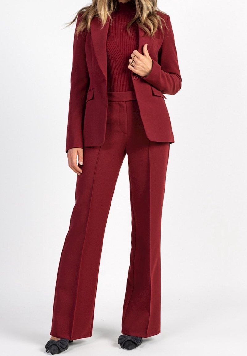 Costume pantalon bordeaux avec un blazer cintré et un top ajusté, présentant un design en maille texturée. Tissu lisse avec pantalon évasé.