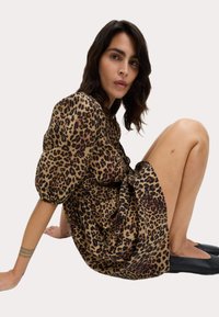 Robe imprimée léopard en tissu léger, avec des manches bouffantes, une taille froncée et qui tombe au-dessus du genou. Des ballerines noires complètent le look.
