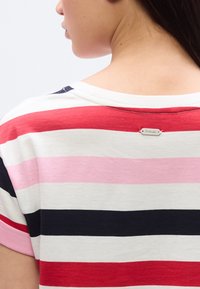 Βαμβακερό τοπ με κο ντά μανίκια και οριζόντιες ρίγες σε κόκκινο, ροζ, λευκό και μπλε ναυτικό. Διαθέτει μικρή ετικέτα στο πίσω μέρος κοντά στη λαιμόκοψη.