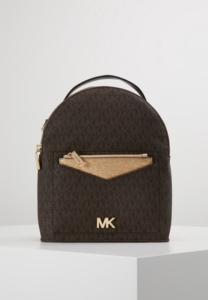 Sac à dos marron Michael Kors avec poche avant dorée et logo MK, posé sur un piédestal blanc sur un fond clair uni.