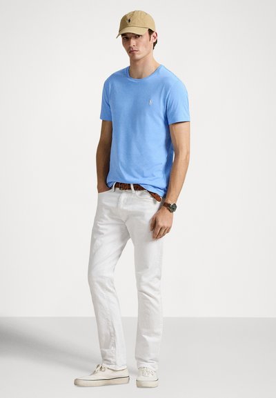 Ανοιχτό μπλε βαμβακερό t-shirt με στρογγυλή λαιμόκοψη, συνδυασμένο με λευκό βαμβακερό παντελόνι και μπεζ καπέλο. Αθλητικά παπούτσια ολοκληρώνουν το casual σύνολο.