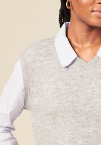 Maglione grigio a maglia indossato sopra una camicia a righe blu chiaro e bianco con colletto, caratterizzato da un design a scollo a V e una texture morbida.
