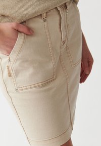 Bežna denim krila z oprijeto zasnovo, zanka za pas in dvema sprednjima žepe. Ima subtilne šive in gladko teksturo.