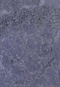 Spitzenstoff zeigt filigrane Blumenmuster in Blautönen, mit gestickten Details und dezenten Pailletten, die Textur und Dimension hinzufügen.