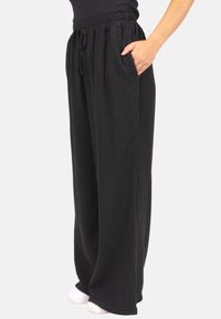 Schwarze, weite Hosen aus strukturiertem Material mit einem elastischen Bund und Kordelzug sowie seitlichen Taschen.
